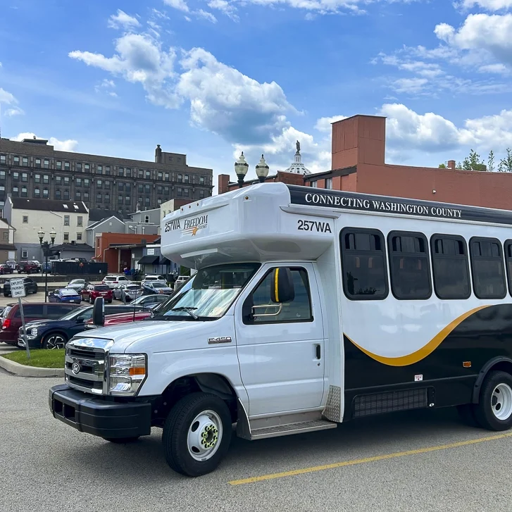 New shared ride bus, bus is white with an orange swirl and black swirl. Sunny day bus parked in a parking lot.